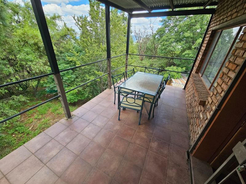 Covered outdoor patio featuring tiled flooring, exposed brickwork, and metal railings, offering an elevated view of the surrounding trees.