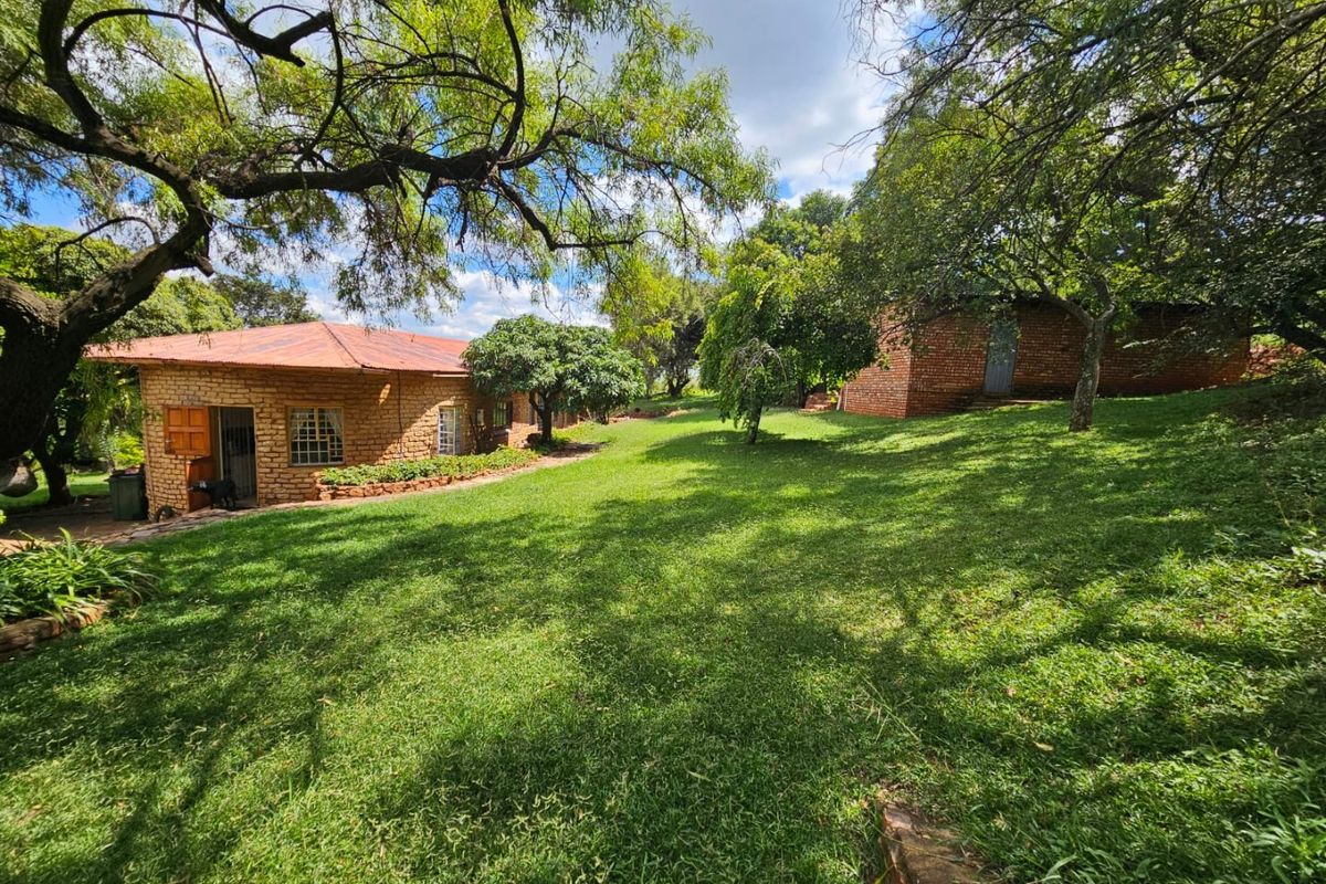 A view of the rear garden featuring mature trees, a well-maintained lawn, and the exposed brick exterior of the farm dwelling.