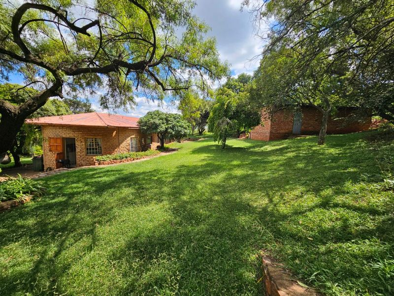 A view of the rear garden featuring mature trees, a well-maintained lawn, and the exposed brick exterior of the farm dwelling.