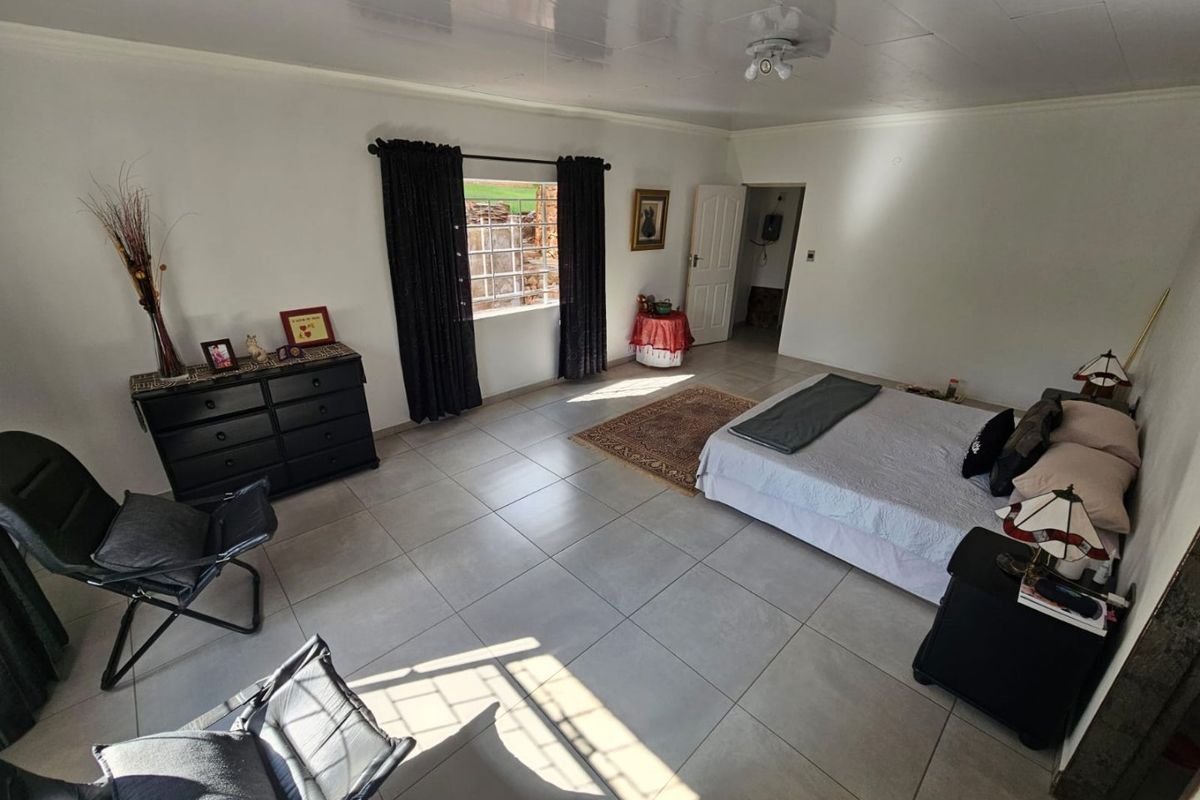 Spacious bedroom featuring neutral tiled flooring, a ceiling fan, and a window with security bars, offering a clean and functional living space.