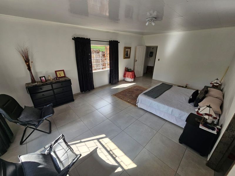 Spacious bedroom featuring neutral tiled flooring, a ceiling fan, and a window with security bars, offering a clean and functional living space.
