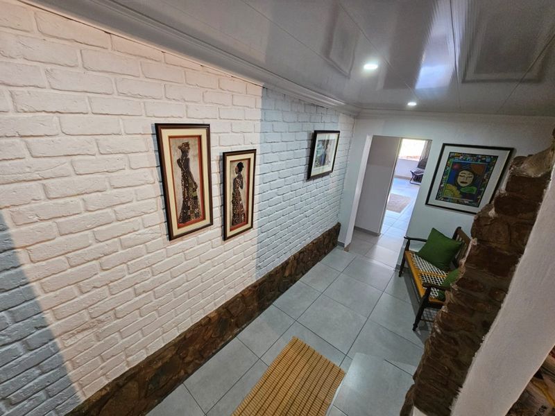 A well-lit hallway featuring white painted exposed brick walls, stone base detailing, and modern tiled flooring leading to an adjacent room.