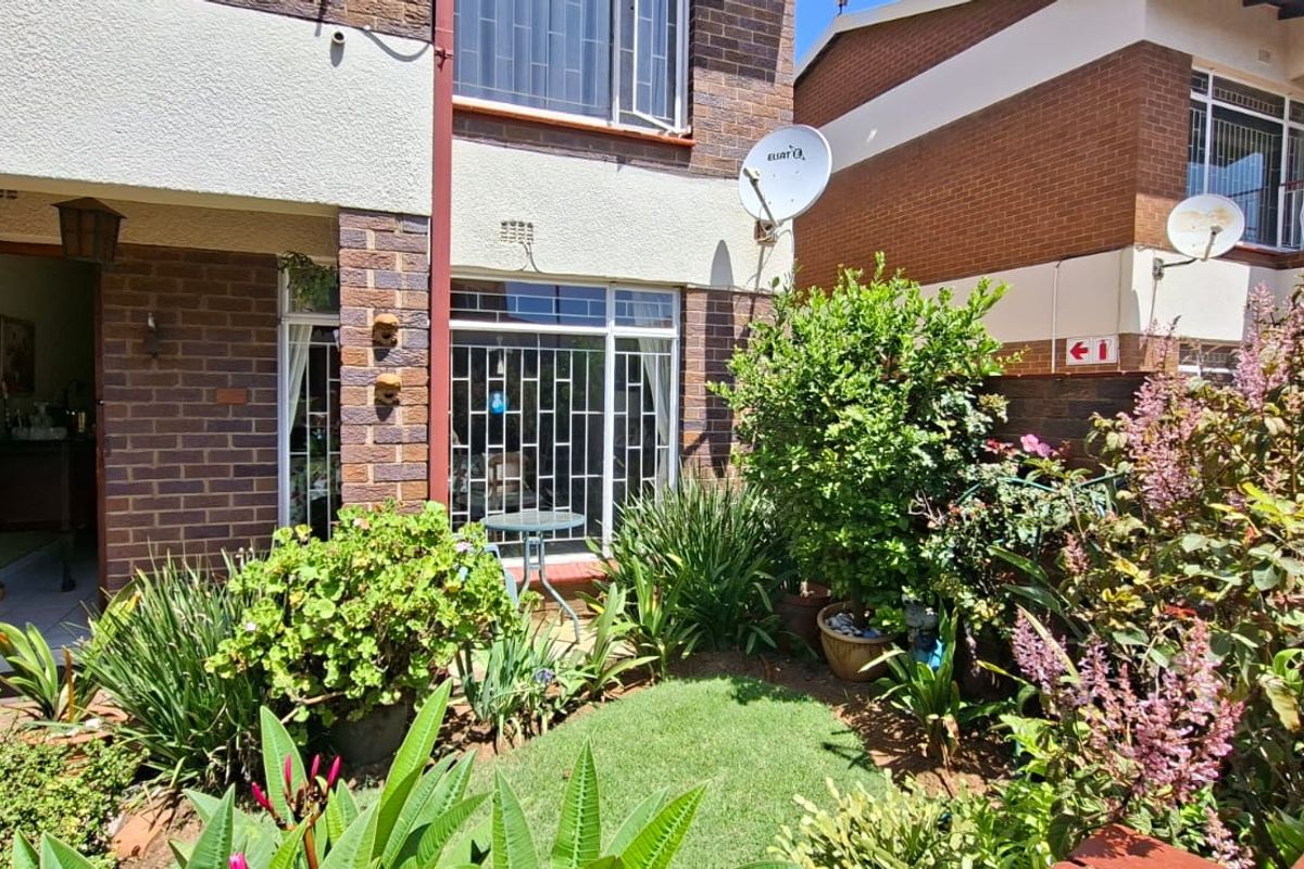 Rear exterior view of the townhouse featuring a private garden, paved patio area, and brick facade with security window bars.