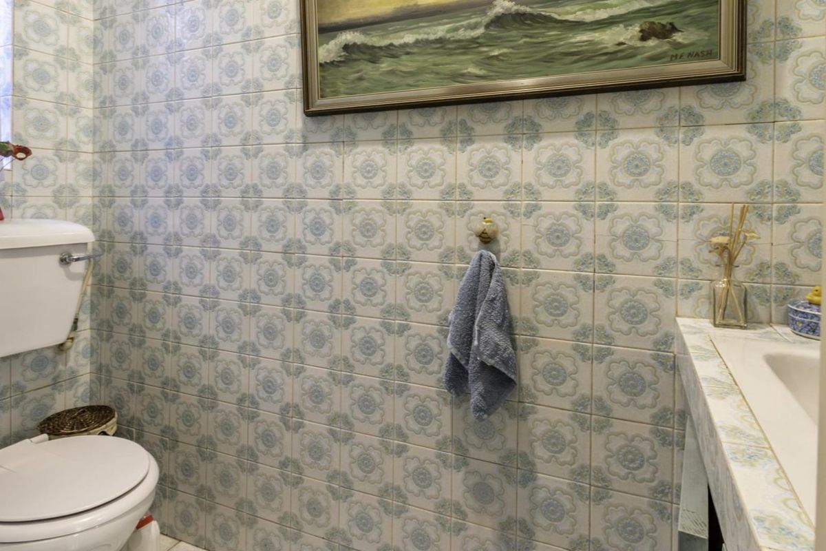 A compact bathroom featuring dated floral patterned wall tiles, a built-in vanity with an integrated sink, and a standard toilet.