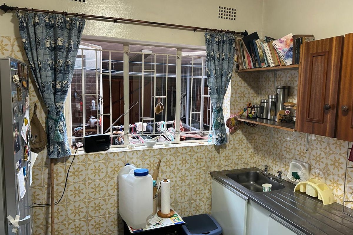 A compact kitchen featuring dated wall tiles, built-in wooden cabinetry, and a stainless steel sink with security bars on the window.