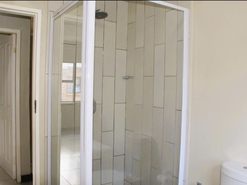 A clean bathroom featuring a glass-enclosed shower with vertical wall tiling and a standard toilet.