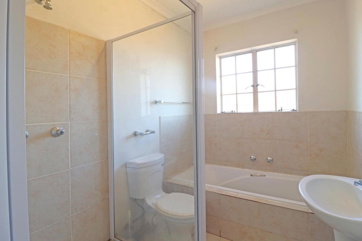 A functional bathroom featuring a separate shower enclosure, built-in bathtub, pedestal basin, and toilet with neutral wall tiling.