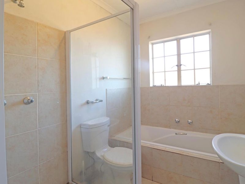 A functional bathroom featuring a separate shower enclosure, built-in bathtub, pedestal basin, and toilet with neutral wall tiling.