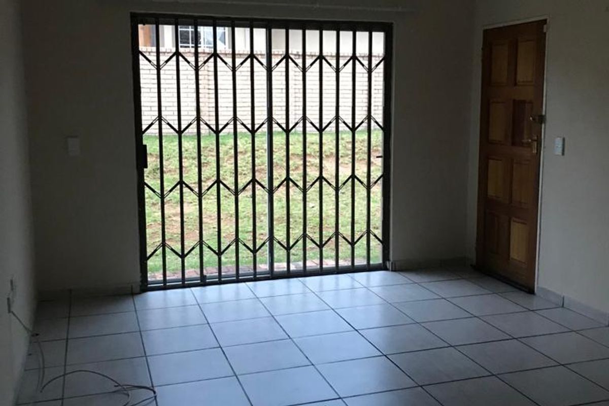 An empty living room featuring tiled flooring, a timber door, and a sliding glass door with a security gate leading to the rear garden.