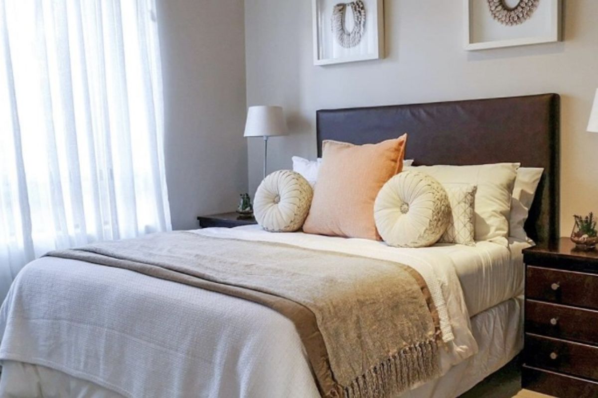 A well-maintained bedroom featuring neutral wall tones, natural light through large windows, and a clean, modern aesthetic.