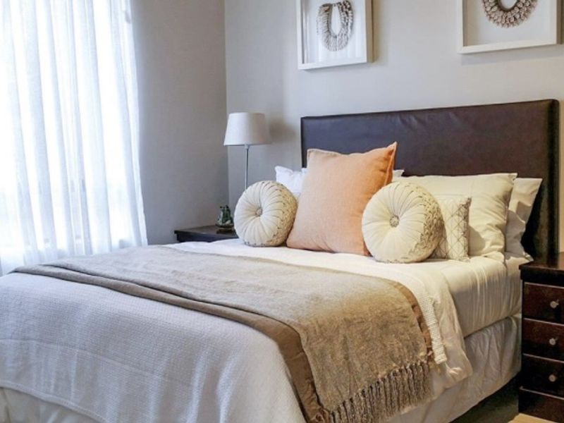 A well-maintained bedroom featuring neutral wall tones, natural light through large windows, and a clean, modern aesthetic.