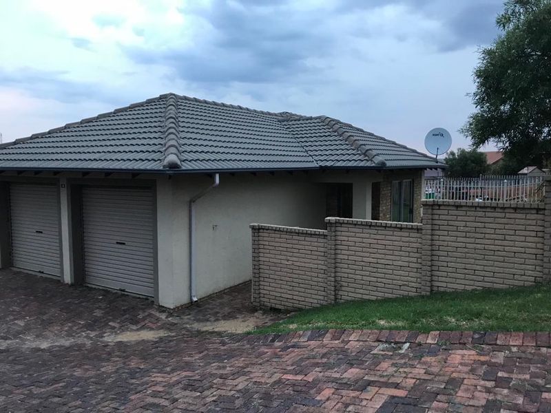 Front view of a townhouse featuring a double garage, paved driveway, and brick boundary wall under a tiled roof.