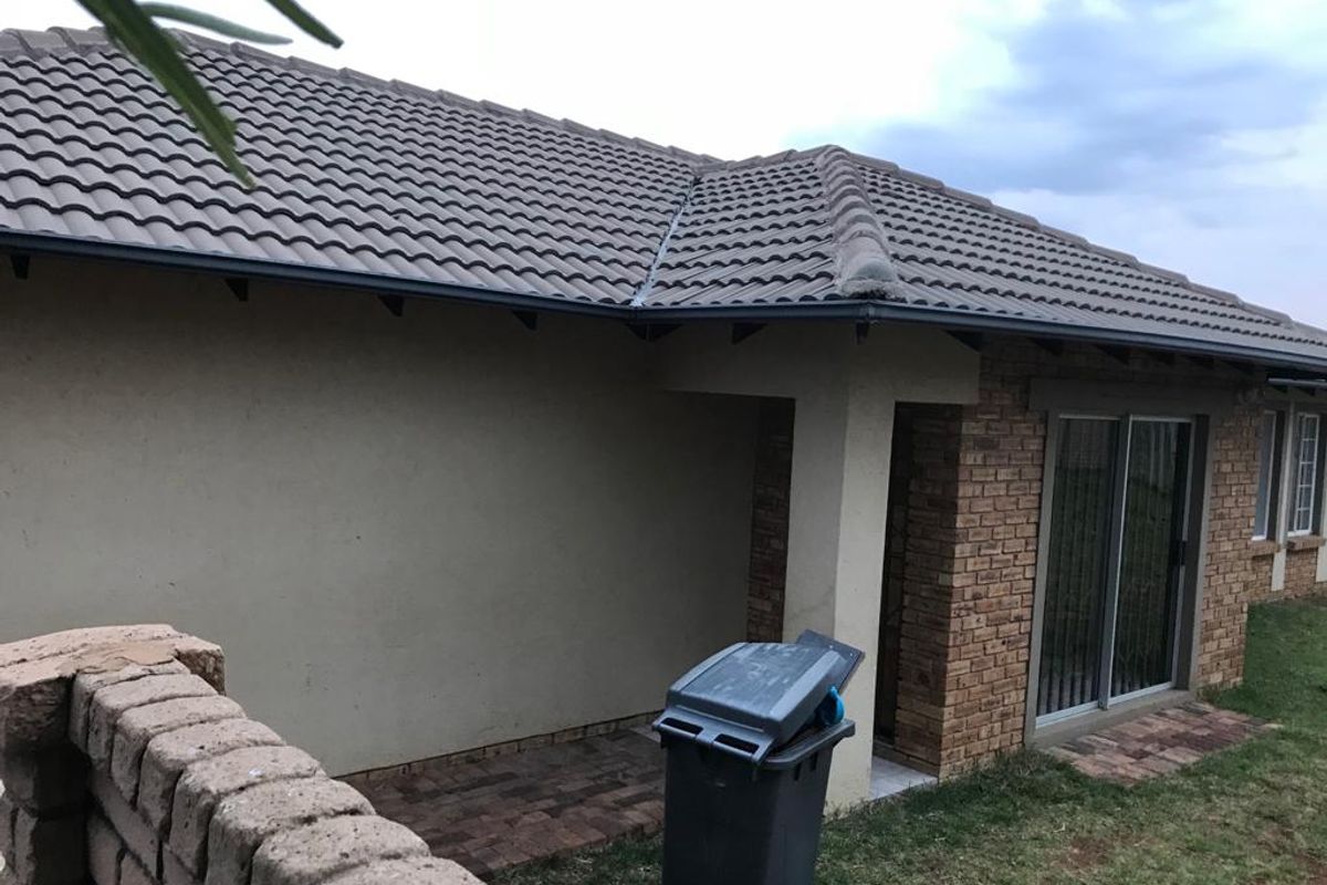Rear view of the townhouse featuring a brick facade, concrete tiled roof, and a paved patio area with sliding glass door access.