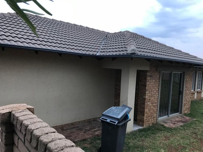 Rear view of the townhouse featuring a brick facade, concrete tiled roof, and a paved patio area with sliding glass door access.