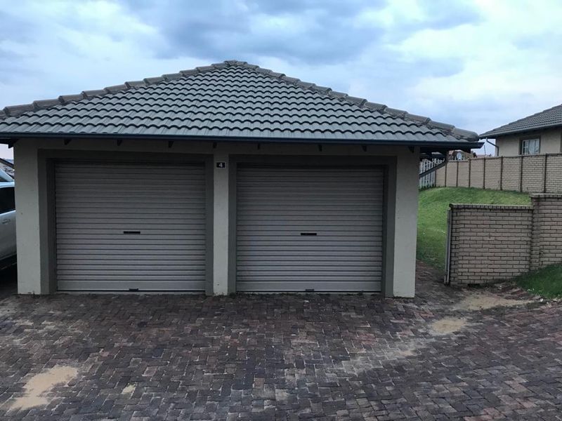 A detached double garage featuring roller doors, a tiled roof, and a brick-paved driveway within a secure residential setting.