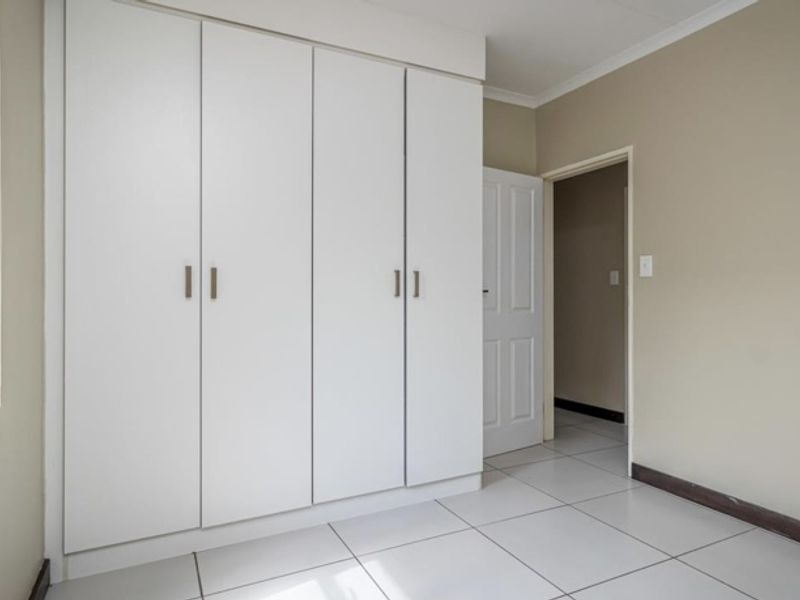 A clean, empty bedroom featuring neutral walls, white built-in cupboards, and tiled flooring, offering a blank canvas for personalization.