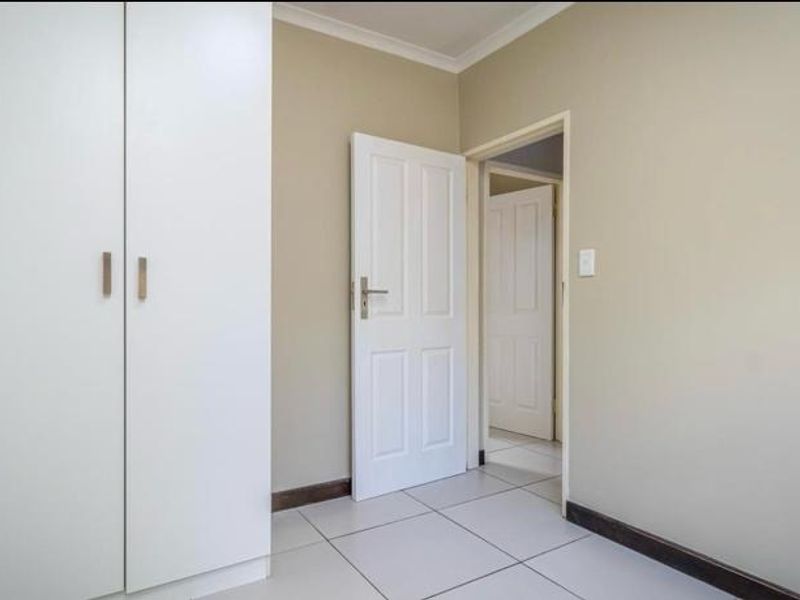 A clean, empty bedroom featuring neutral walls, tiled flooring, and built-in cupboards, offering a versatile space ready for personalization.