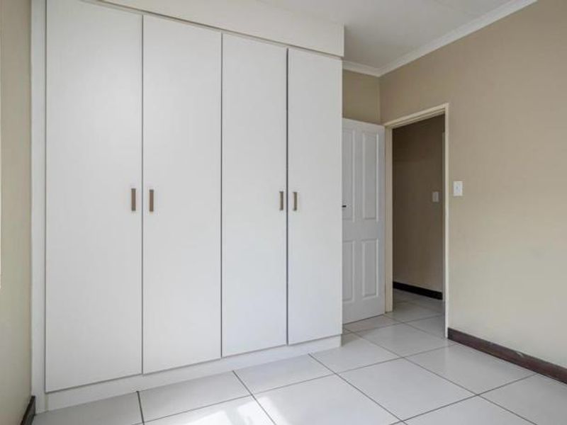 A clean, empty bedroom featuring neutral wall tones, white built-in cupboards, and light-colored floor tiles, offering a versatile space ready for personalization.