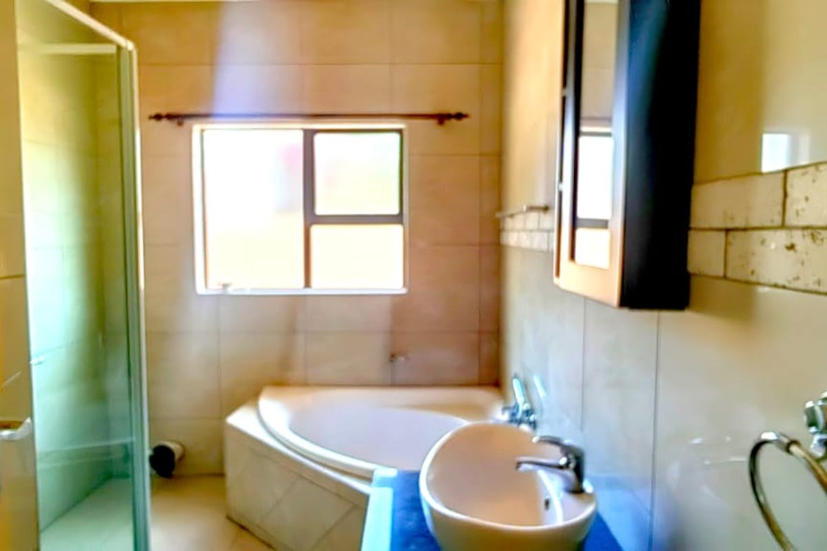 A functional bathroom featuring a corner bathtub, a separate glass-enclosed shower, and a vanity basin with wall-mounted storage.