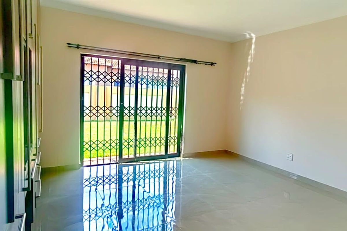 A bright, empty bedroom featuring built-in cupboards, tiled flooring, and a sliding glass door with a security gate leading to the garden.