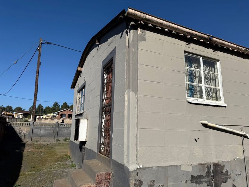 Rear exterior view of a concrete block house featuring security gates, window bars, and visible exterior wall maintenance requirements.