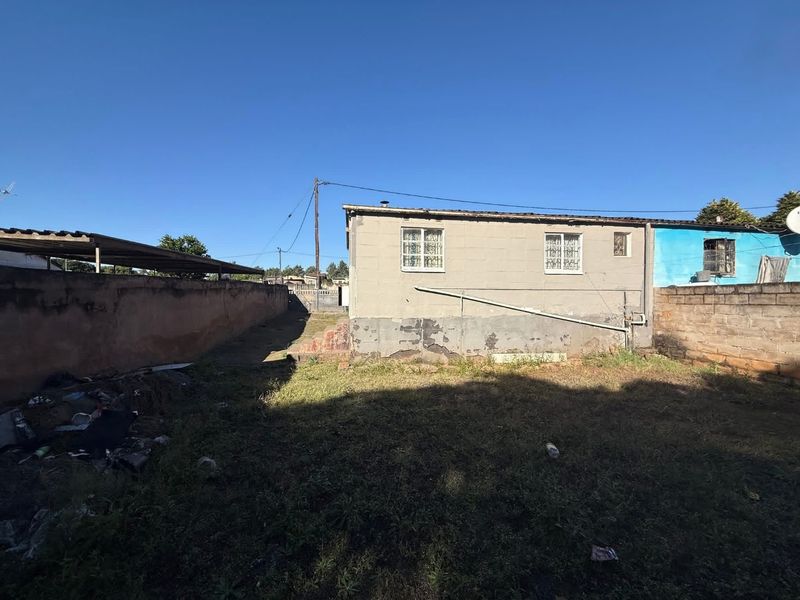 Rear view of the property showing a concrete block structure with security bars on windows and a surrounding perimeter wall.