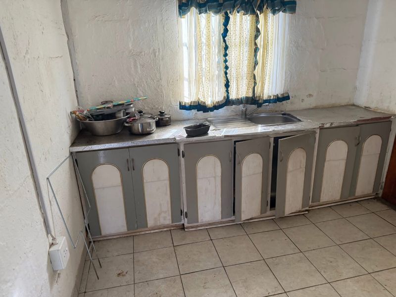 A dated kitchen area featuring a stainless steel sink, tiled flooring, and worn built-in cabinetry in need of renovation.