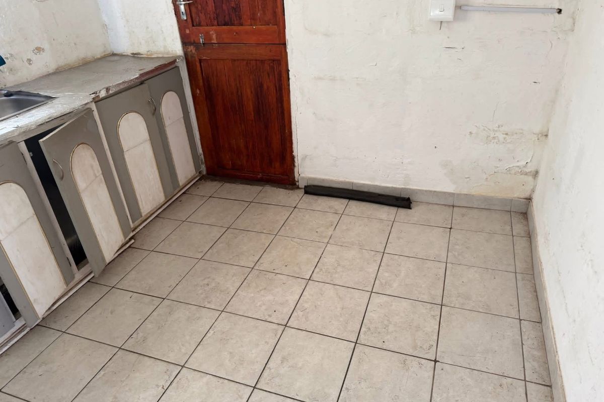 A small kitchen area featuring tiled flooring, basic cabinetry, and a stainless steel sink, requiring significant cosmetic updates and repairs.