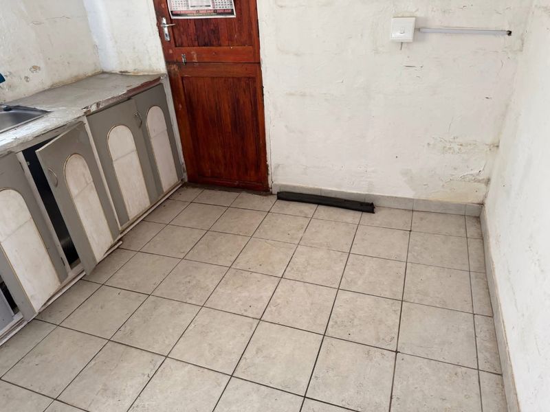 A small kitchen area featuring tiled flooring, basic cabinetry, and a stainless steel sink, requiring significant cosmetic updates and repairs.