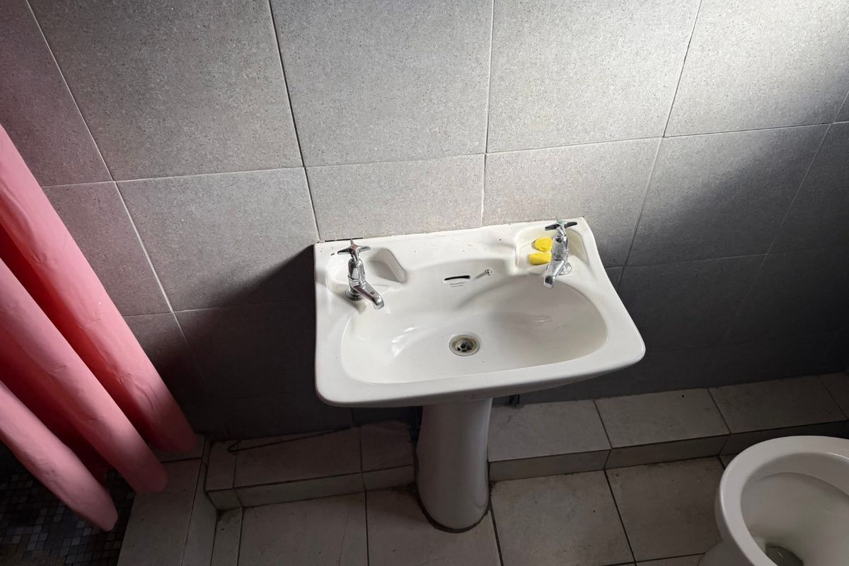 A functional bathroom featuring a pedestal basin, tiled walls, and floor tiles, currently in need of cosmetic updates and maintenance.
