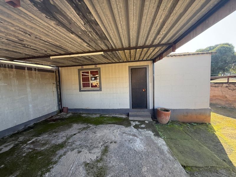 A covered outdoor parking area or garage featuring a corrugated metal roof, concrete flooring, and cinder block construction.