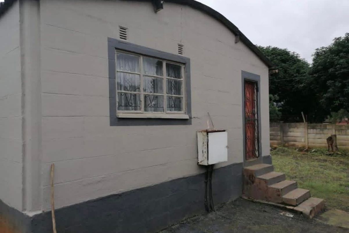 Rear exterior view of the house featuring concrete block walls, a security gate, and external electrical infrastructure.