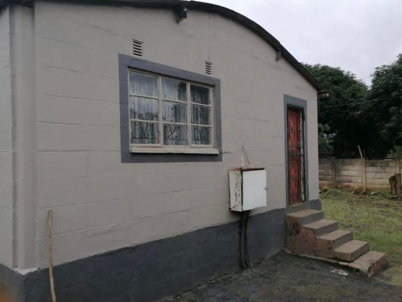 Rear exterior view of the house featuring concrete block walls, a security gate, and external electrical infrastructure.