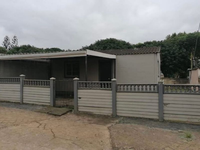 Front view of a single-story house featuring a covered patio, enclosed by a precast concrete boundary wall and gate with a concrete driveway.