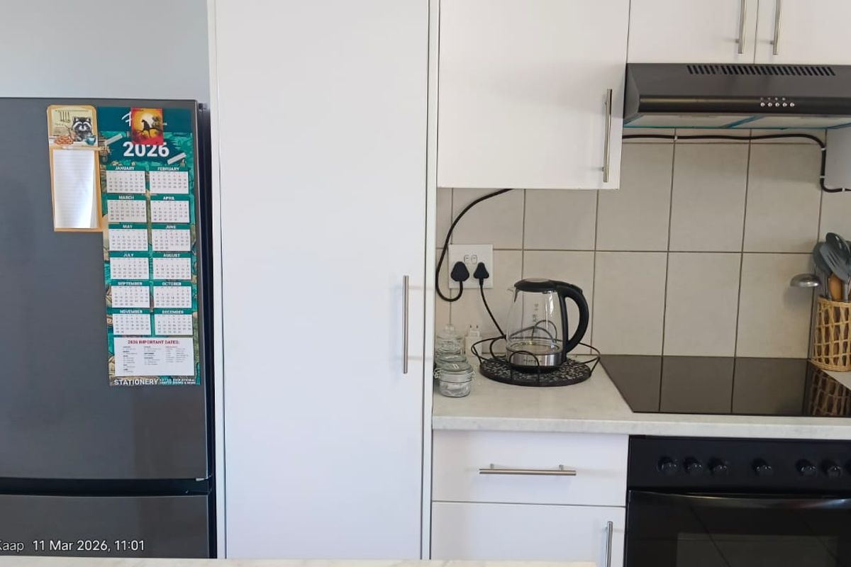 A functional kitchen featuring white cabinetry, a laminate countertop, ceramic tile backsplash, and integrated appliances including an electric hob, oven, and extractor fan.