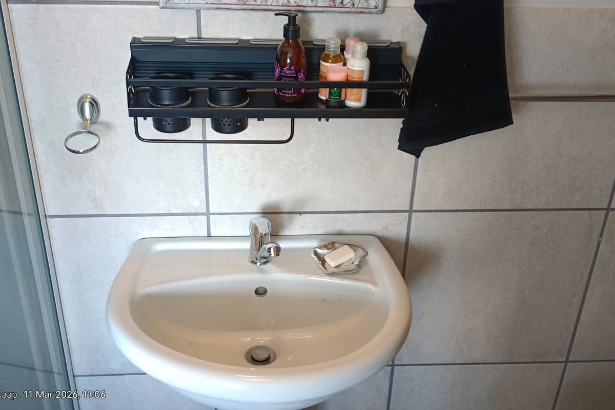 A functional bathroom featuring a wall-mounted basin with a chrome mixer tap, tiled walls, and a glass shower enclosure.