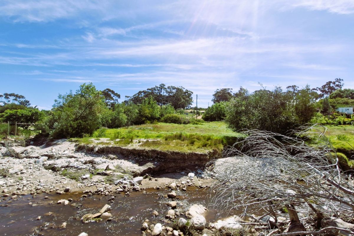 A view of the vacant residential land featuring a natural watercourse and surrounding vegetation, showing signs of soil erosion along the riverbank.