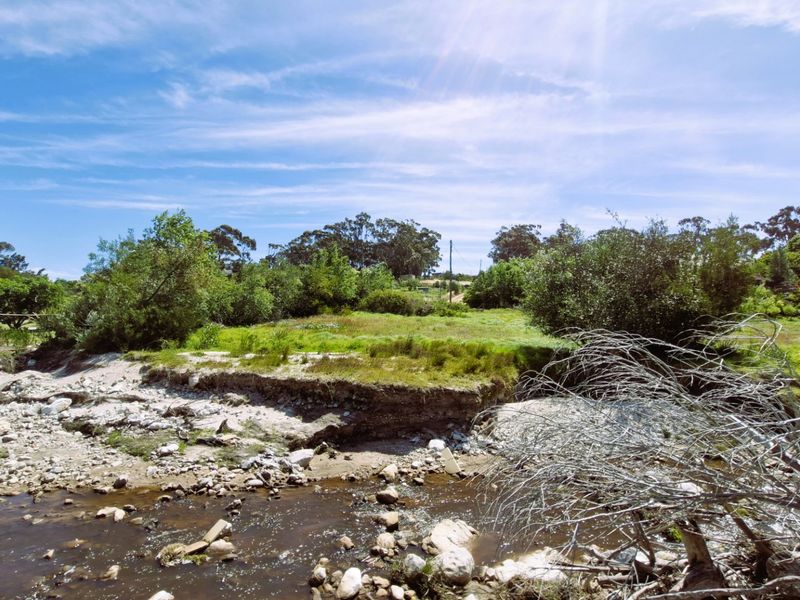 A view of the vacant residential land featuring a natural watercourse and surrounding vegetation, showing signs of soil erosion along the riverbank.