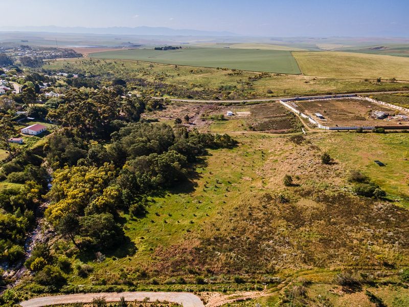 An aerial view of a large, undeveloped residential land parcel featuring natural vegetation, a river, and surrounding rural landscape.