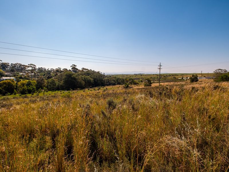 A wide-angle view of the vacant residential land, featuring natural vegetation and distant landscape views under a clear blue sky.
