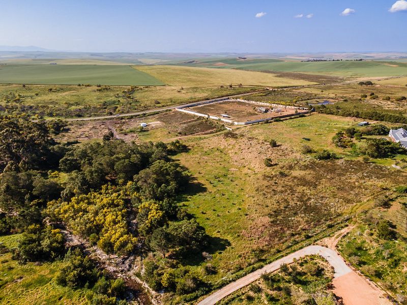 Aerial view of a large vacant residential plot featuring natural landscape, perimeter walling, and access road in a rural setting.