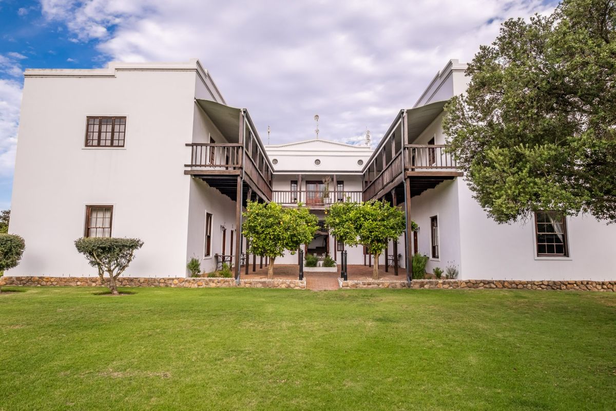 A well-maintained farm estate featuring a symmetrical white facade with timber balconies, sash windows, and a central courtyard area.