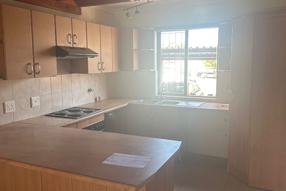 A functional kitchen featuring light wood cabinetry, laminate countertops, an electric hob with extractor, and exposed timber ceiling beams.