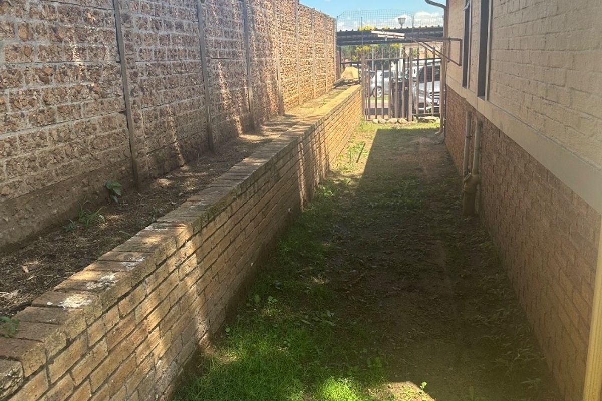 A narrow side passage of the townhouse featuring brick boundary and retaining walls, with access to a rear security gate.