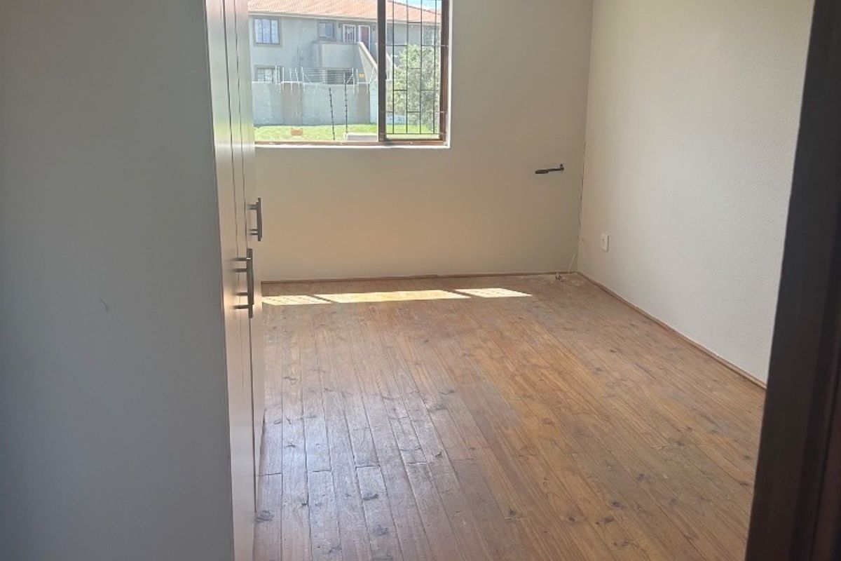 An empty bedroom featuring timber flooring, built-in cupboards, and an air conditioning unit, offering a blank canvas for personalization.