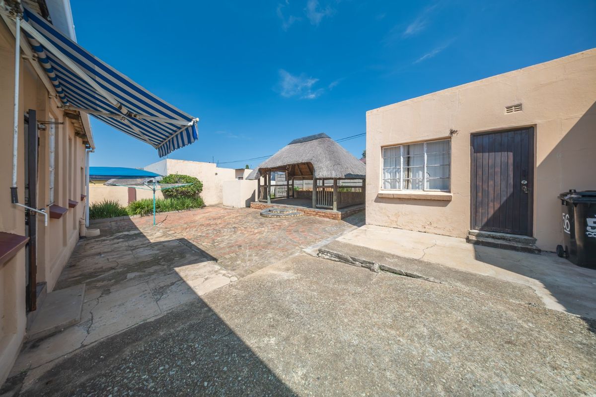 Rear courtyard featuring a thatched gazebo, brick paving, and a retractable awning, providing a functional outdoor entertainment space.
