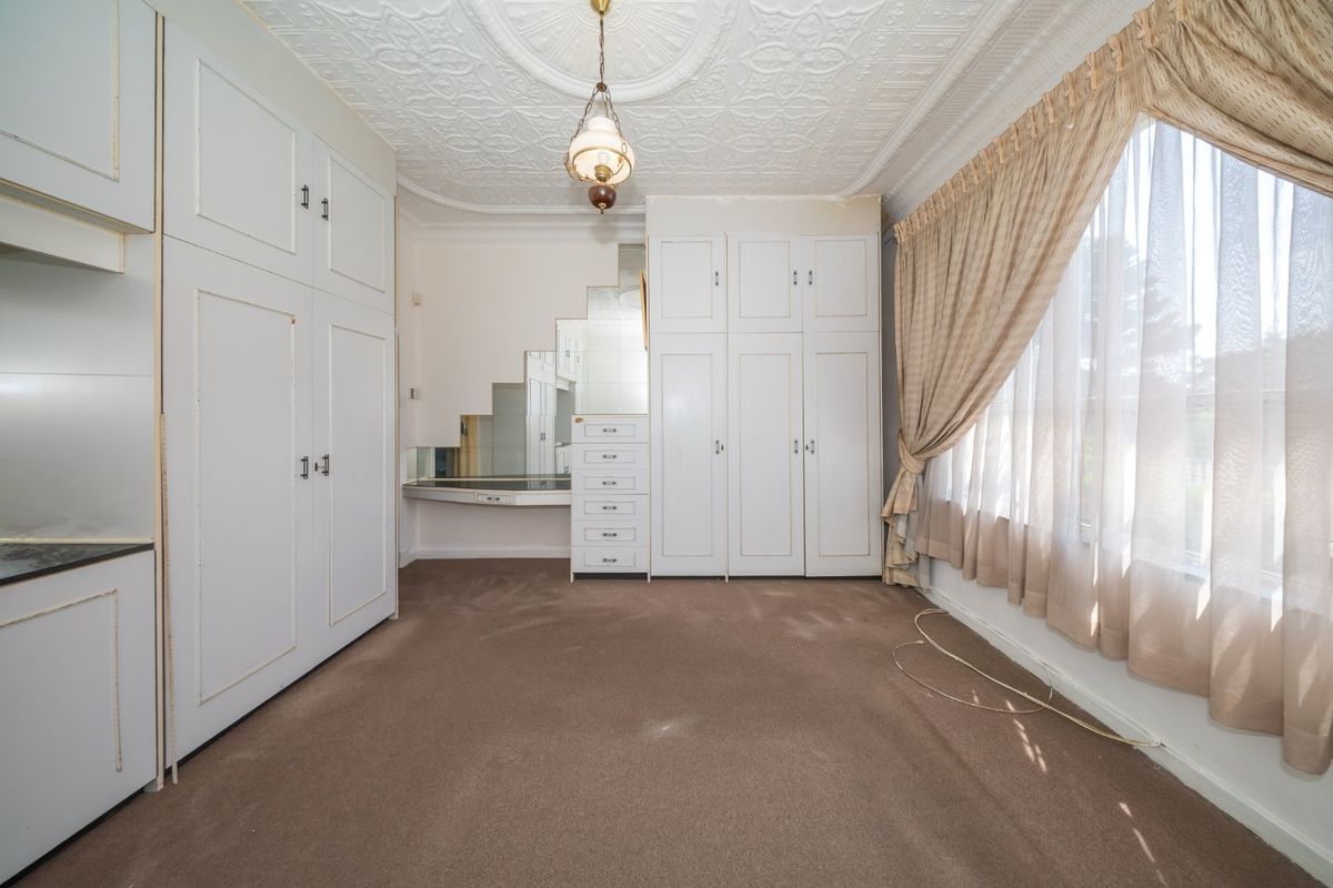 Spacious bedroom featuring extensive built-in cabinetry, a integrated vanity with mirrored splashback, and a decorative pressed metal ceiling.