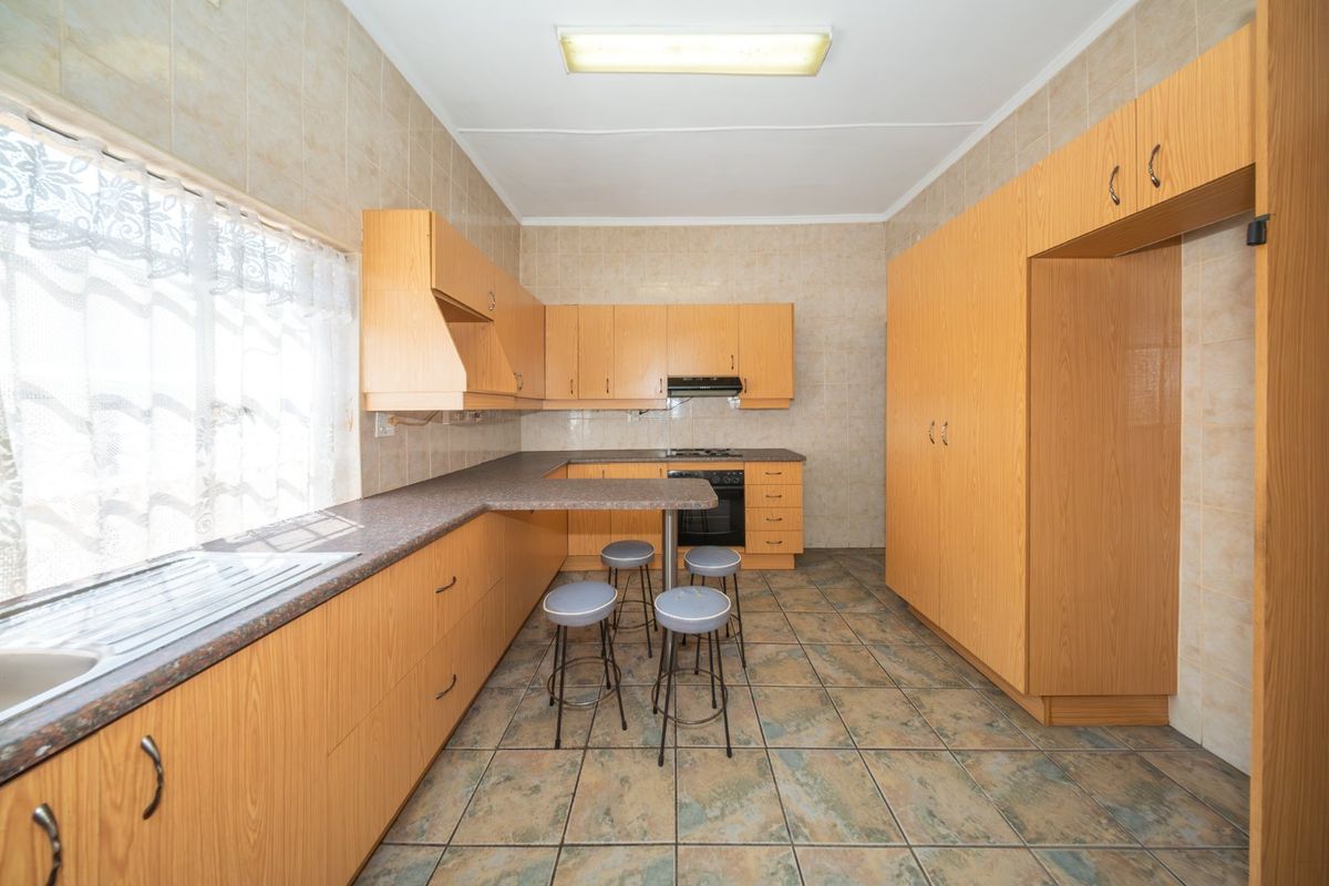 A functional kitchen featuring laminate cabinetry, tiled walls and flooring, built-in oven, hob, and extractor fan with a breakfast bar area.