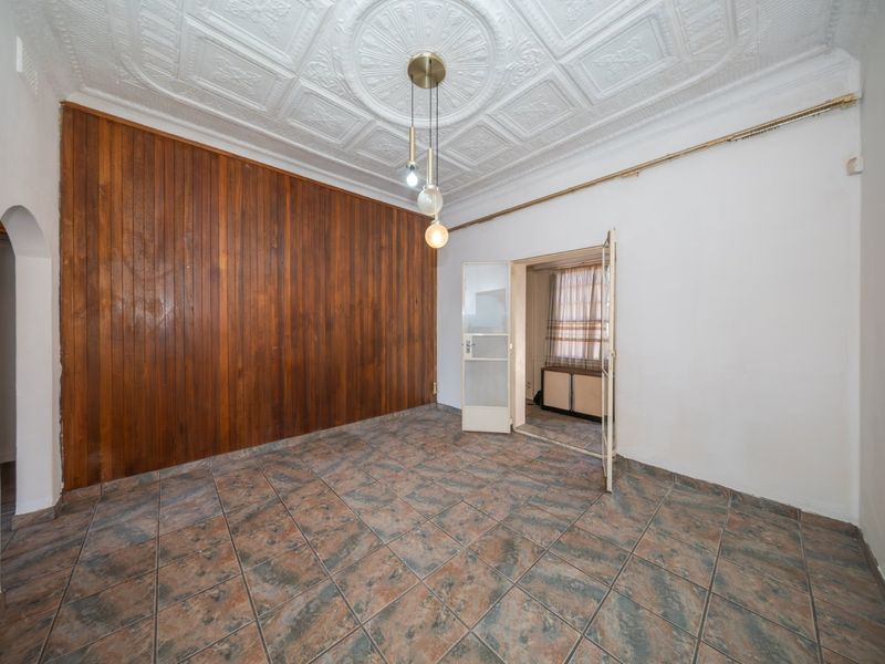 An empty living room featuring a decorative pressed metal ceiling, timber wall paneling, and ceramic floor tiles, offering a blank canvas for renovation.