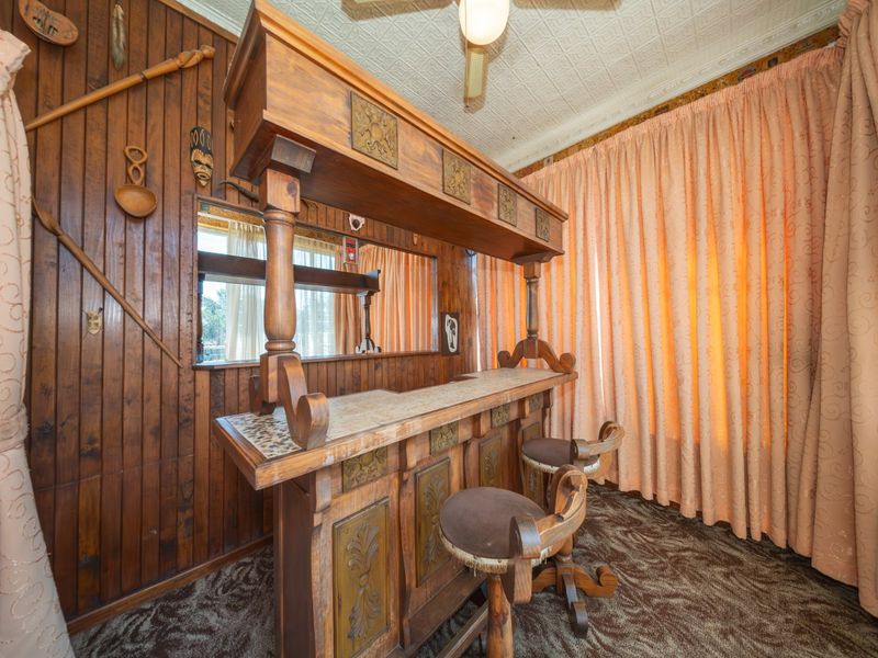 A dedicated bar area featuring built-in wooden cabinetry, decorative ceiling tiles, and wood-paneled walls, offering a classic, dated aesthetic.